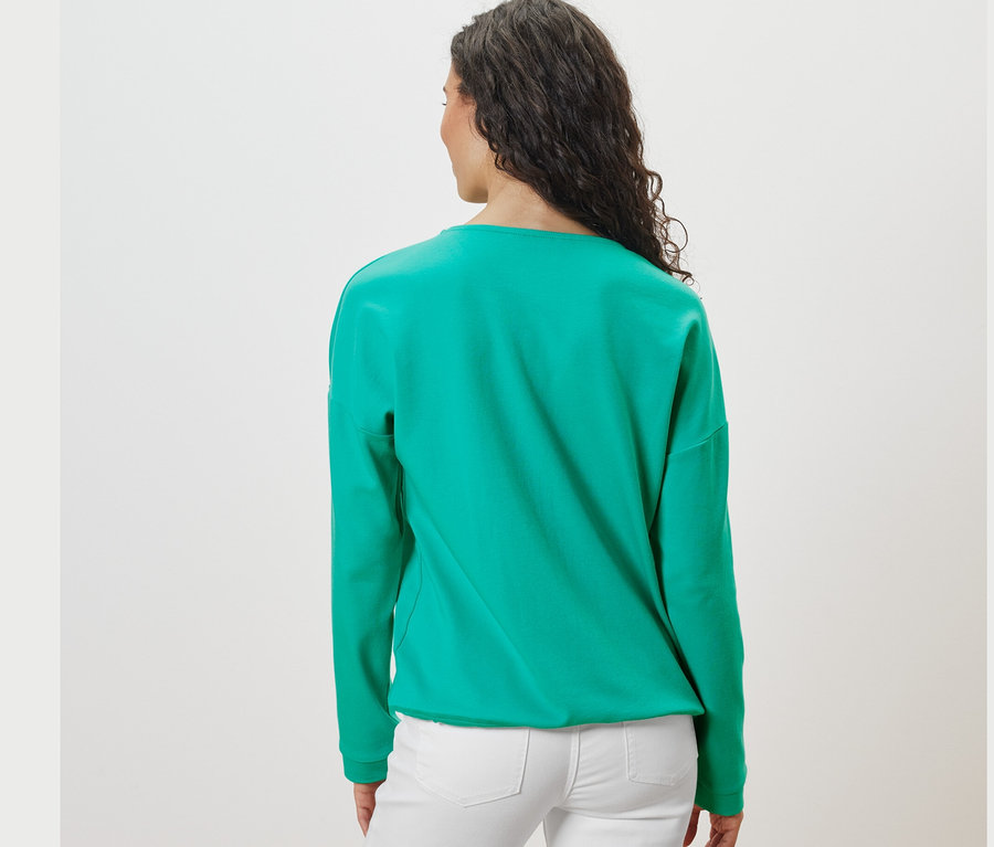 Rückansicht einer Frau mit dunklen Haaren in einem aquafarbenen Sweatshirt.