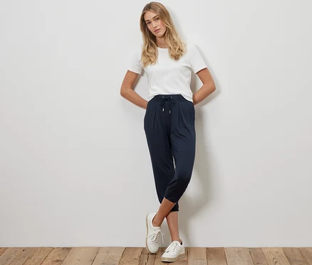 Blonde Frau posiert in dunkelblauer 3/4-Jerseyhose und weißem T-Shirt.