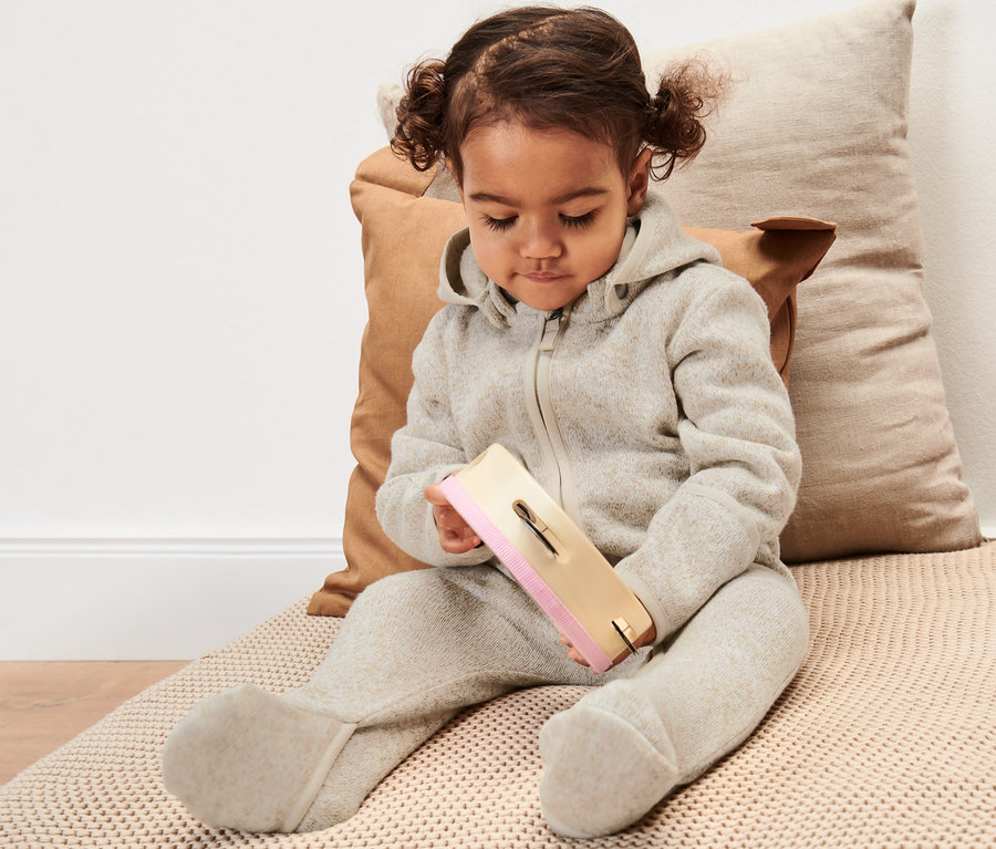 Kleinkind sitzt und spielt mit Spielzeug, es trägt einen Baby-Strickfleece-Overall.