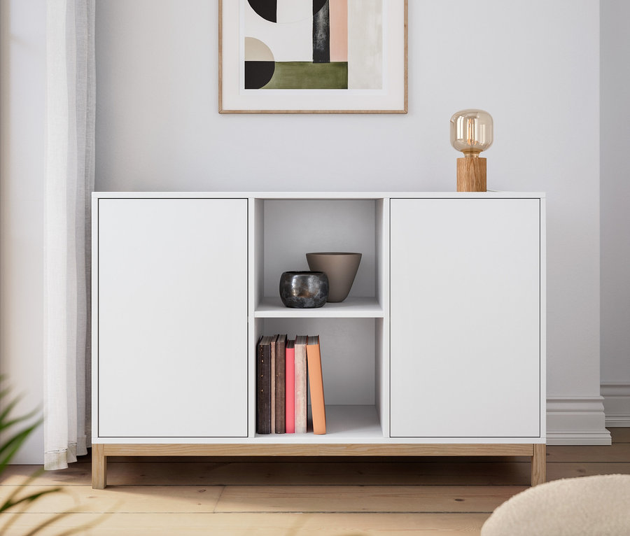 Weißes Sideboard mit Tischleuchte aus Holz. An der Wand hängt ein Bild.
