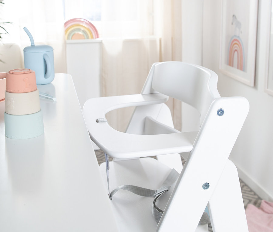 Weißer roba Treppenhochstuhl Sit Up Flex steht an einem weißen Tisch, auf dem pastellfarbenes Spielzeug steht.