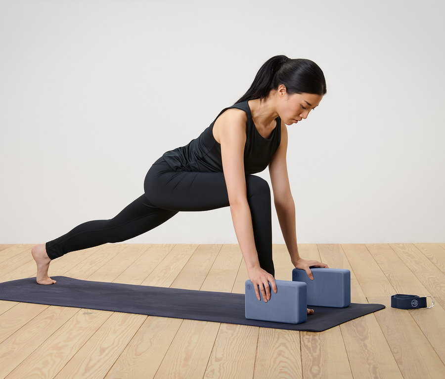 Frau macht Yoga-Übung mit Yoga-Set, das zwei Blöcke und einen Gurt beinhaltet.