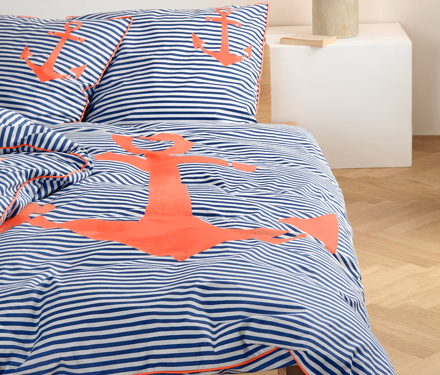 Gestreifte Perkal-Bettwäsche mit Ankermotiv auf einem Bett.