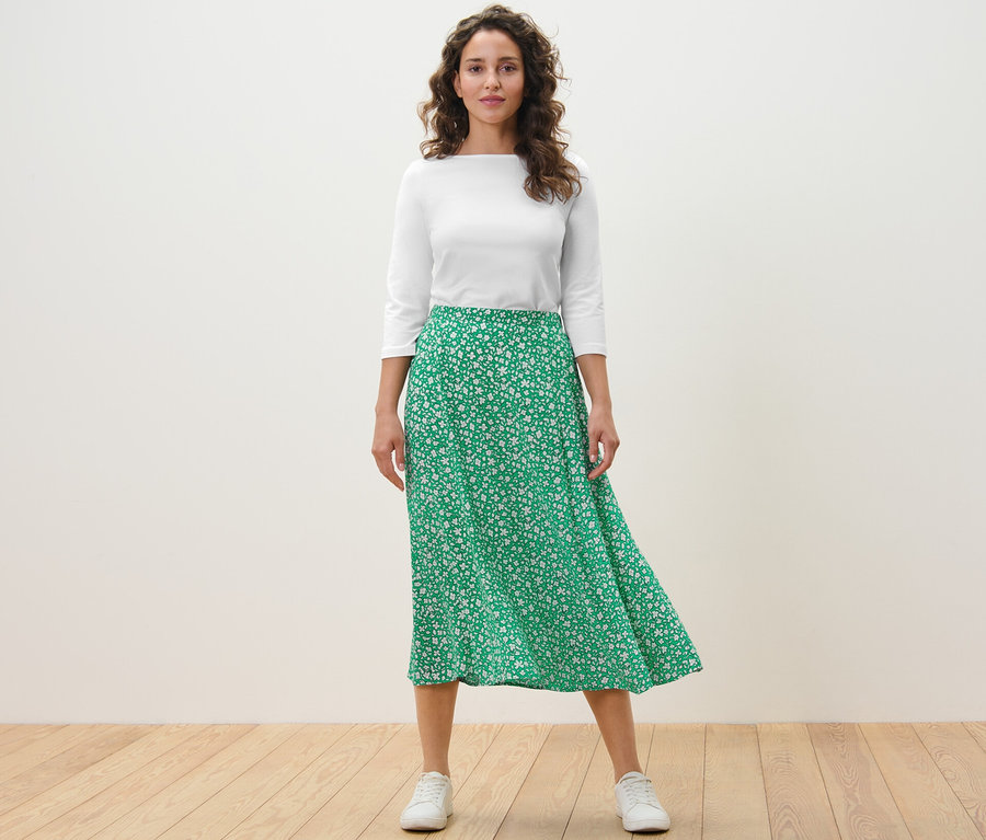 Frau steht und trägt einen bedruckten Midirock, grün.