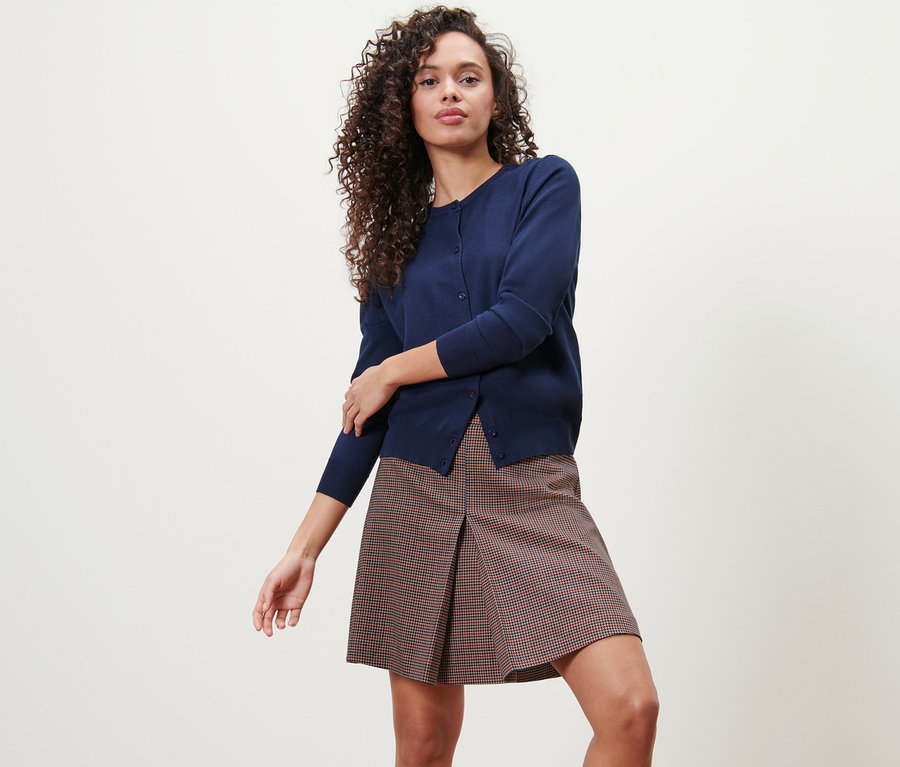 Frau posiert in kariertem Webrock und Strickjacke.