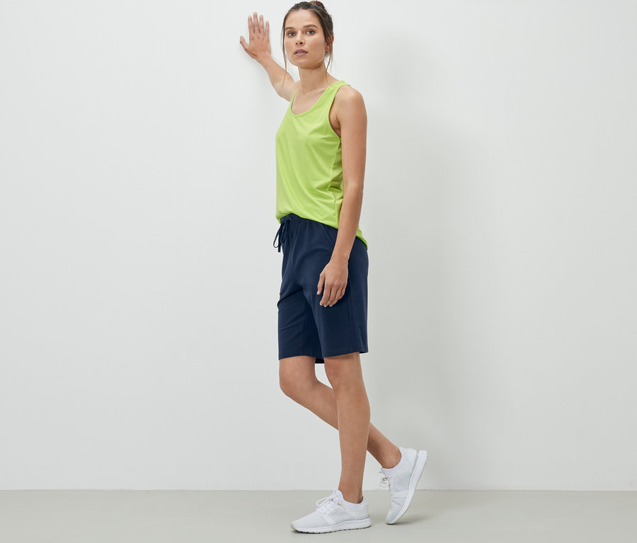 Eine Frau, die sich an eine Wand lehnt, trägt dunkelblaue Sweatshorts.