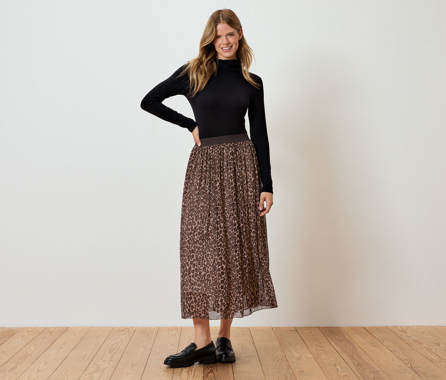 Frau steht und posiert in schwarzer Rollkragenbluse und braunem Leopardenrock.