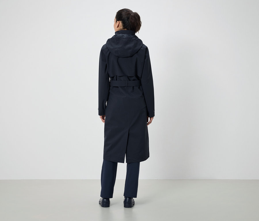 Von hinten ist eine Frau mit einem Pferdeschwanz zu sehen, die einen dunkelblauen Mantel mit Kapuze und Gürtel sowie eine dunkelblaue Hose trägt.