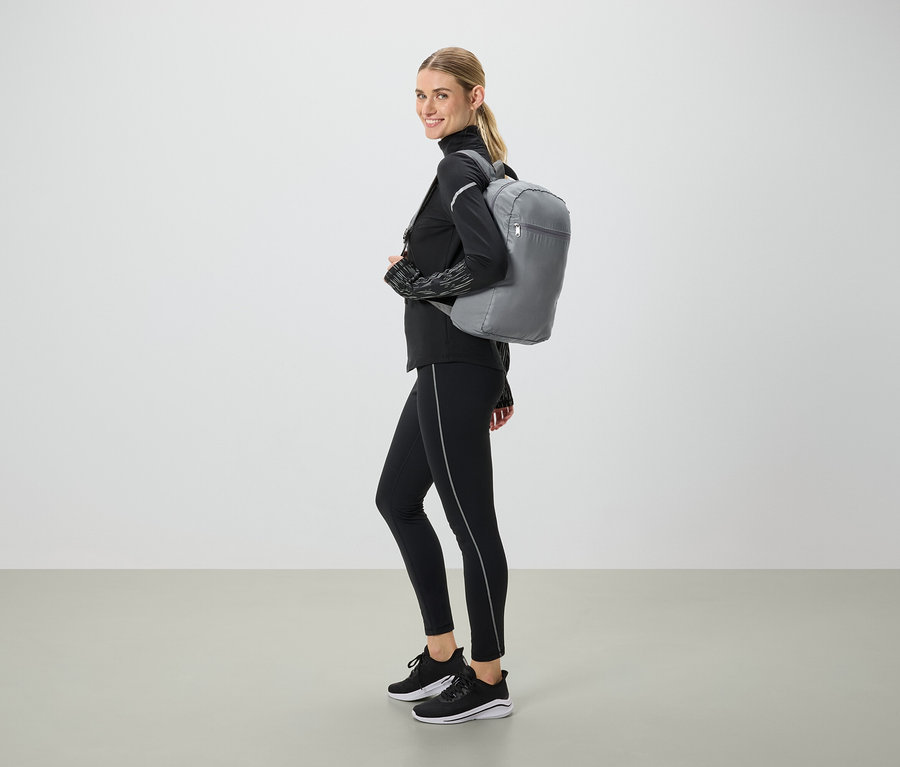 Frau in schwarzer Sportbekleidung mit grauem Rucksack blickt über die Schulter.