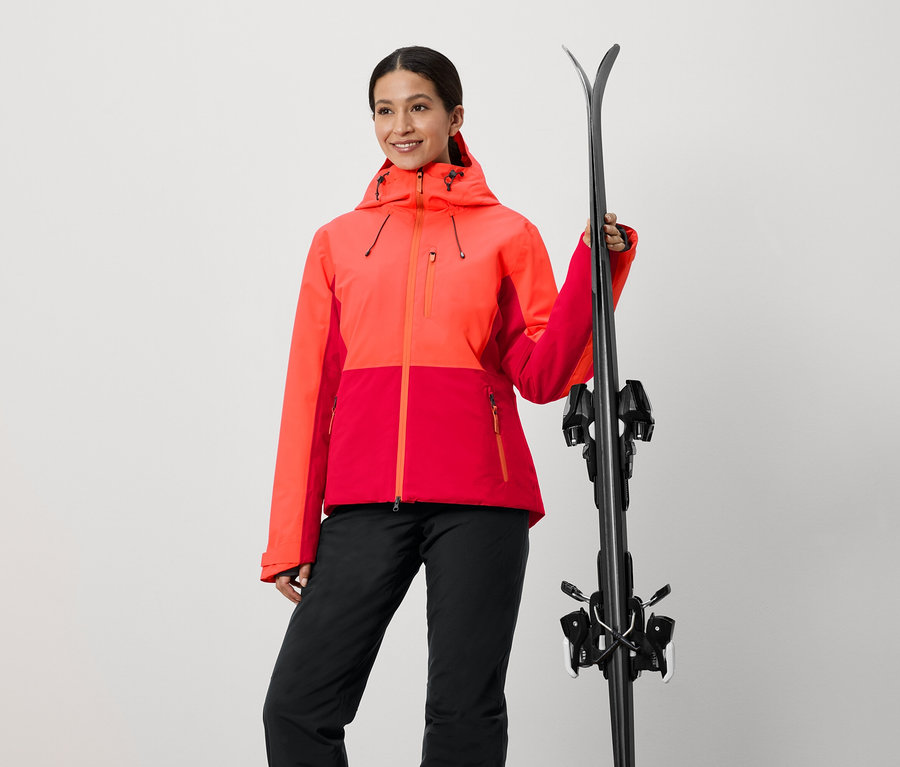 Frau in rot-oranger Jacke hält Ski.