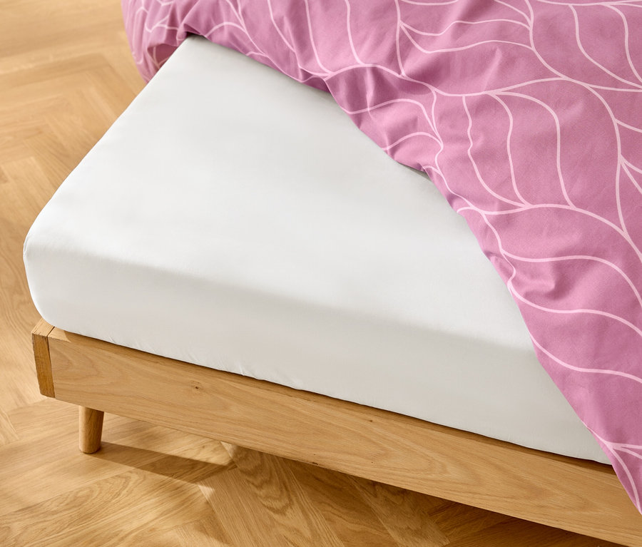 Weisses Spannbettlaken auf einem Holzbettgestell mit rosa Bettwäsche mit weissem Muster.