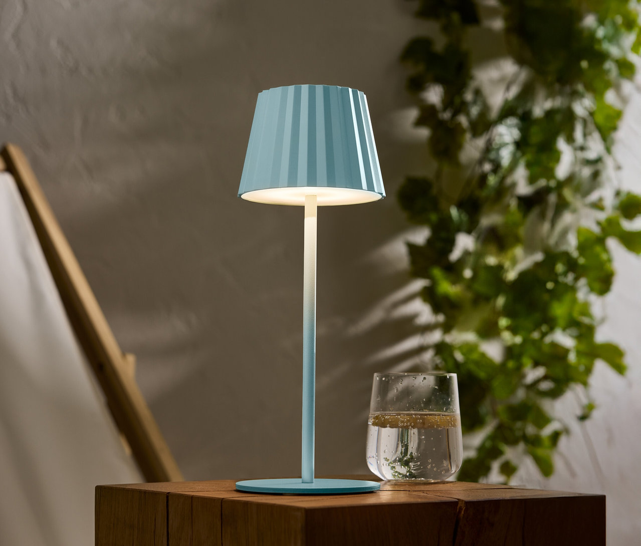 Eine blau gestreifte Lampe steht auf einem Holztisch, daneben ein Glas Wasser.