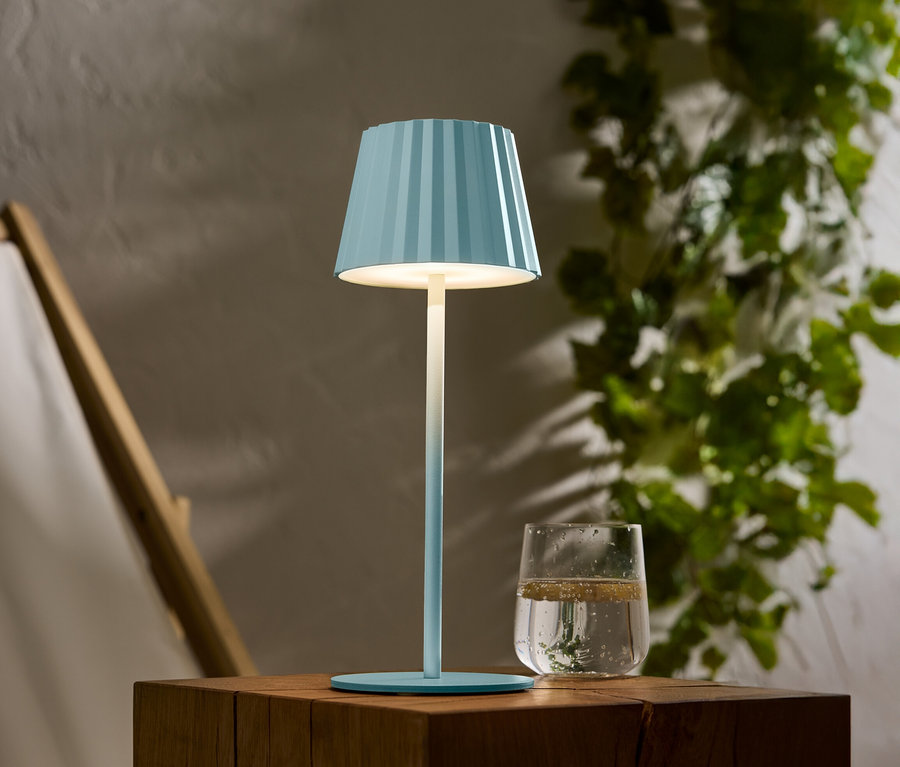 Eine blau gestreifte Lampe steht auf einem Holztisch, daneben ein Glas Wasser.