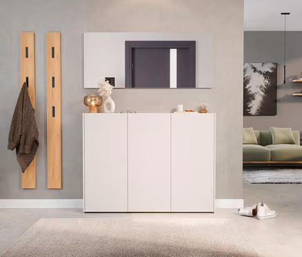 Flur mit weißem Schuhschrank unter rechteckigem Spiegel, zwei Holzgarderobenpaneelen und beigem Teppich.
