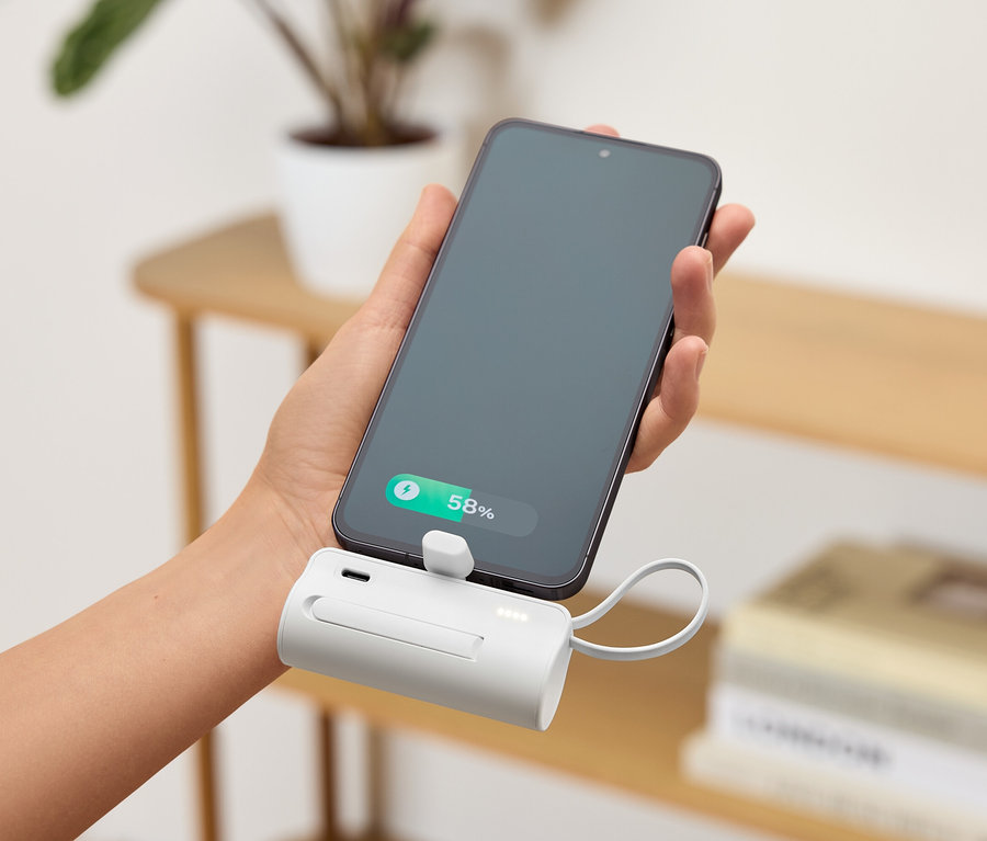 Hand hält ein Smartphone, das an einem weißen, tragbaren Ladegerät befestigt ist. Der Akkustand des Telefons beträgt 58%.