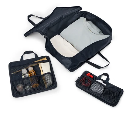 Drei geöffnete, marineblaue Reisetaschen mit Griffen und Reißverschlüssen liegen aufgereiht auf einem weißen Hintergrund. Die Taschen enthalten Kleidung, Kosmetika und Zubehör.