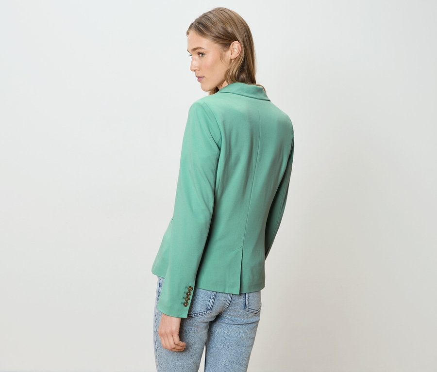 Frau von hinten, trägt einen grünen Blazer und Jeans.