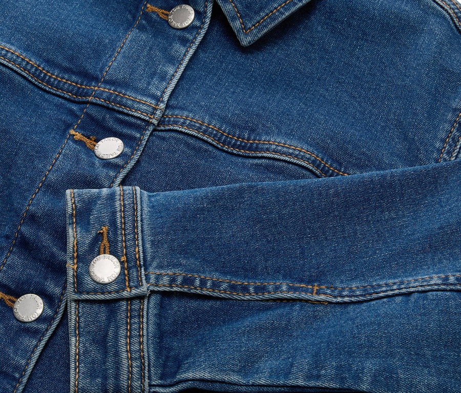 Nahaufnahme einer blauen Jeansjacke mit silbernen Knöpfen.