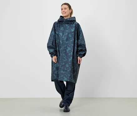 Eine Frau steht in einem langen, blauen Regenponcho mit Kapuze und einem Blattmuster.