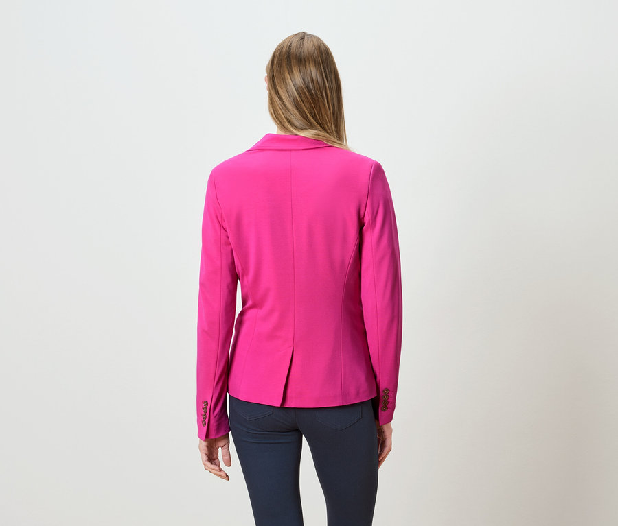 Rückansicht einer Frau mit langen blonden Haaren, die einen pinkfarbenen Blazer und dunkle Jeans trägt.