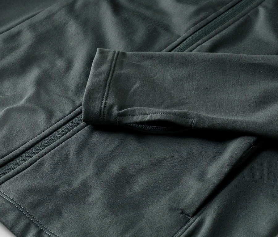 Nahaufnahme einer dunkelgrauen Jacke mit Reißverschluss und Daumenlöchern am Ärmel.