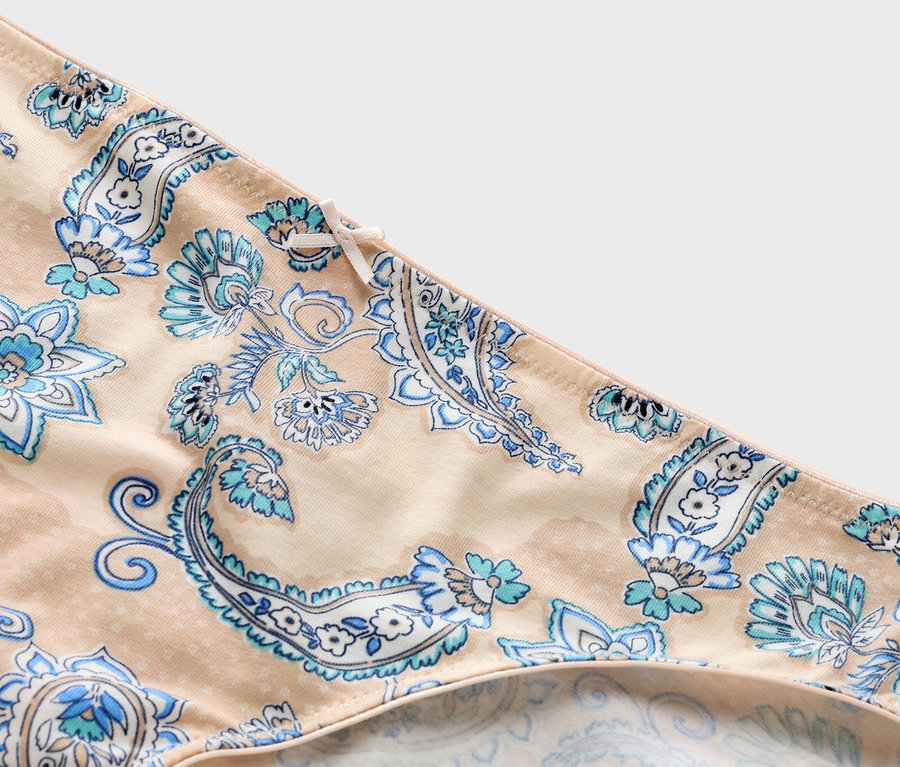 Nahaufnahme eines beigen Slips mit blauem Paisleymuster und Schleife.