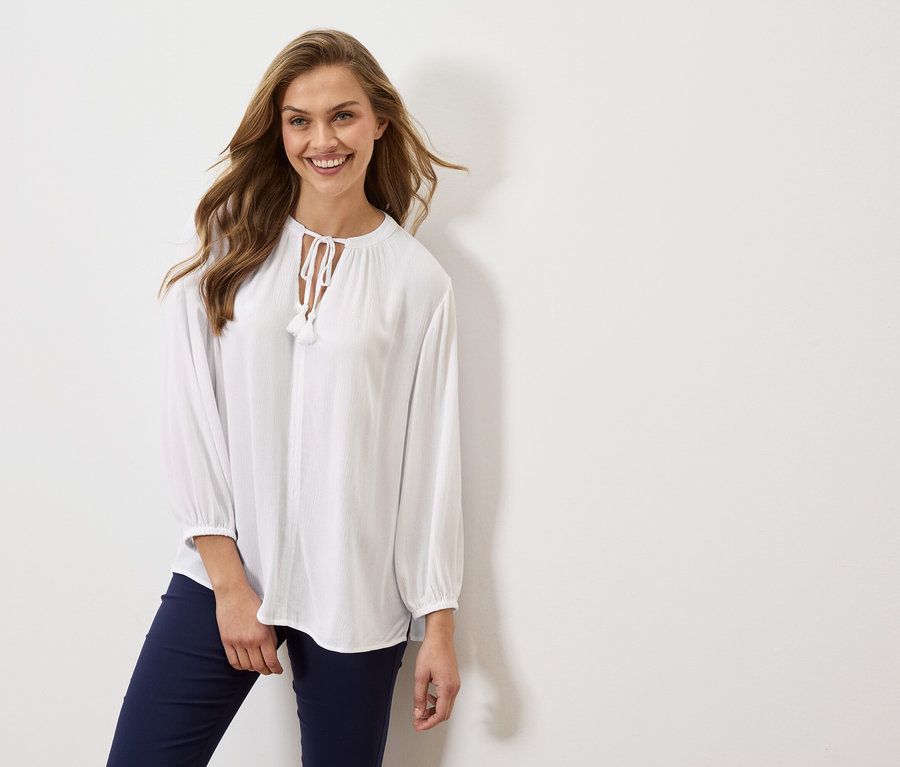 Frau trägt eine weiße Bluse mit langen Ärmeln und marineblaue Hosen.