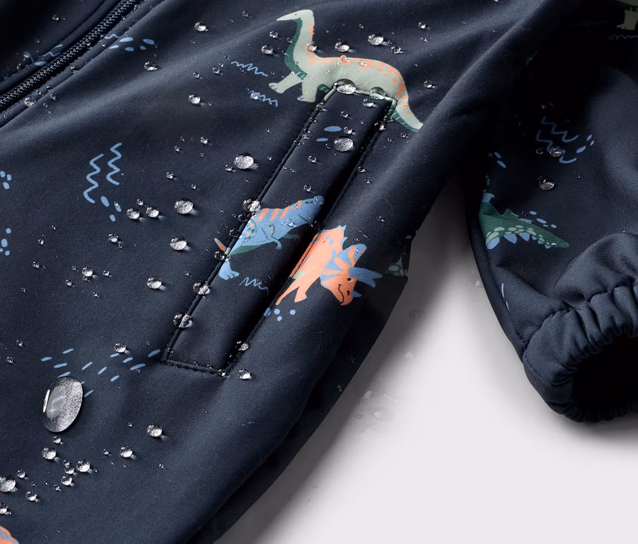 Nahaufnahme einer dunkelblauen Jacke mit Dinosaurier-Muster und Wassertropfen.