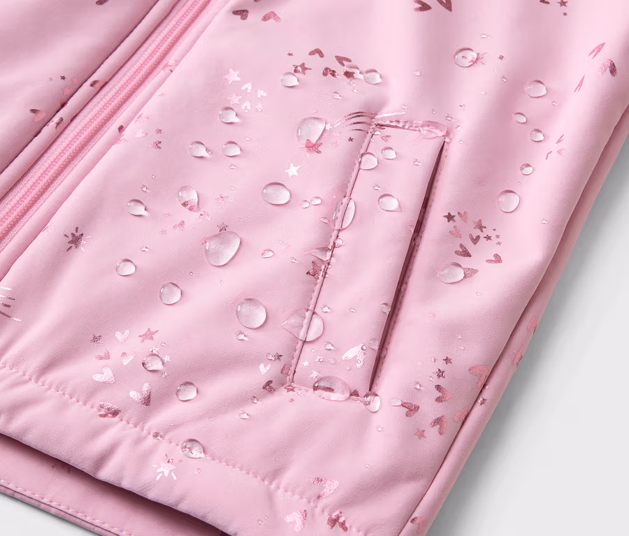 Nahaufnahme einer wasserabweisenden, hellrosa Jacke mit Reißverschluss und Tasche, die mit Herzen und Sternen bedruckt ist.