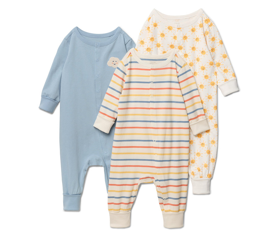 Drei Baby-Schlafanzüge liegen nebeneinander: einfarbig hellblau mit Wolkenapplikation, gestreift in Gelb-, Blau- und Orangetönen sowie weiß mit gelben Sonnen.