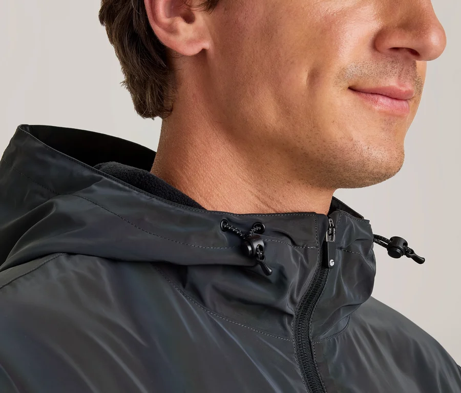 Nahaufnahme eines Mannes im Profil, der eine dunkle, leicht schillernde Jacke mit Kapuze, Reißverschluss und Kordelzug trägt.