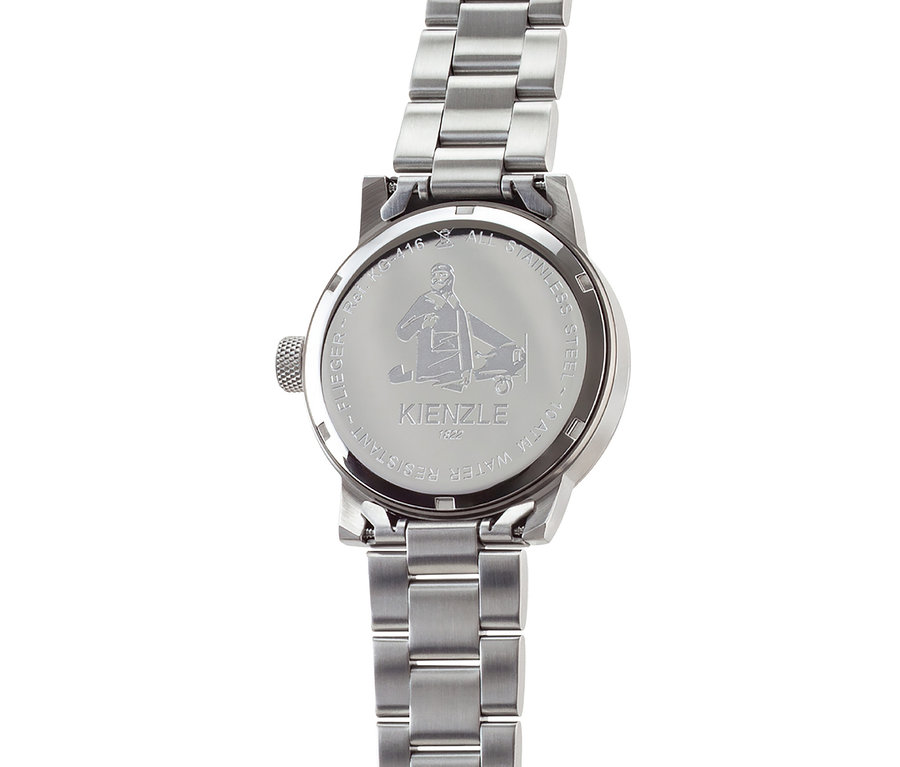 Nahaufnahme der Rückseite einer silberfarbenen Metalluhr mit Metallgliederarmband. Auf dem Gehäuseboden sind ein Flieger und ein Flugzeug sowie die Aufschriften "FLIEGER - Ref. KG-416", "ALL STAINLESS STEEL", "10 ATM WATER RESISTANT", "KIENZLE" und "1822" eingraviert.