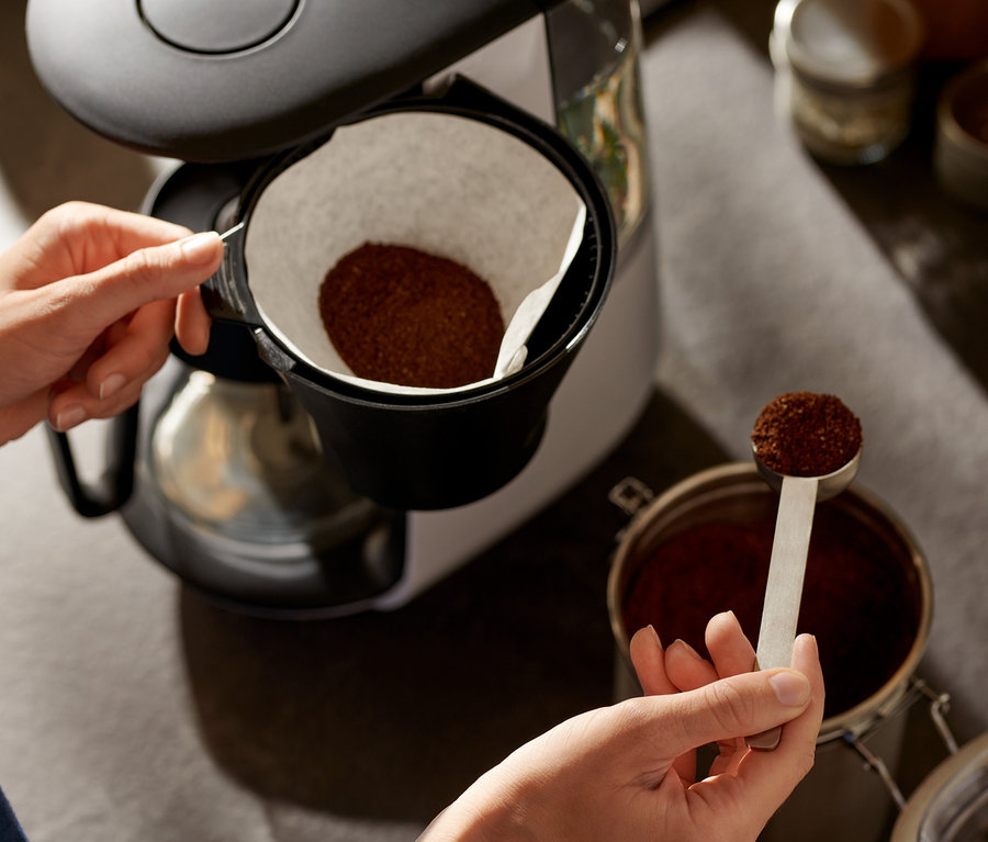 Frau gibt Kaffee in eine weiße »Let's Brew« Filterkaffeemaschine.