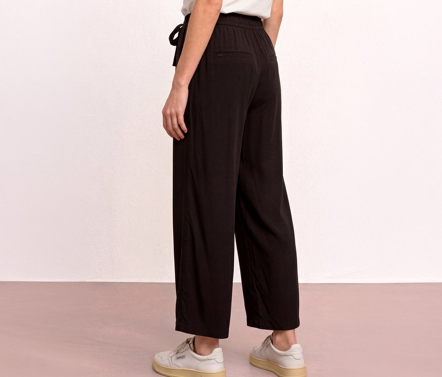 Eine Person steht mit dem Rücken zur Kamera und trägt eine schwarze Street One 7/8-Culotte »EMMA« mit Kordelzug und weiße Sneaker.