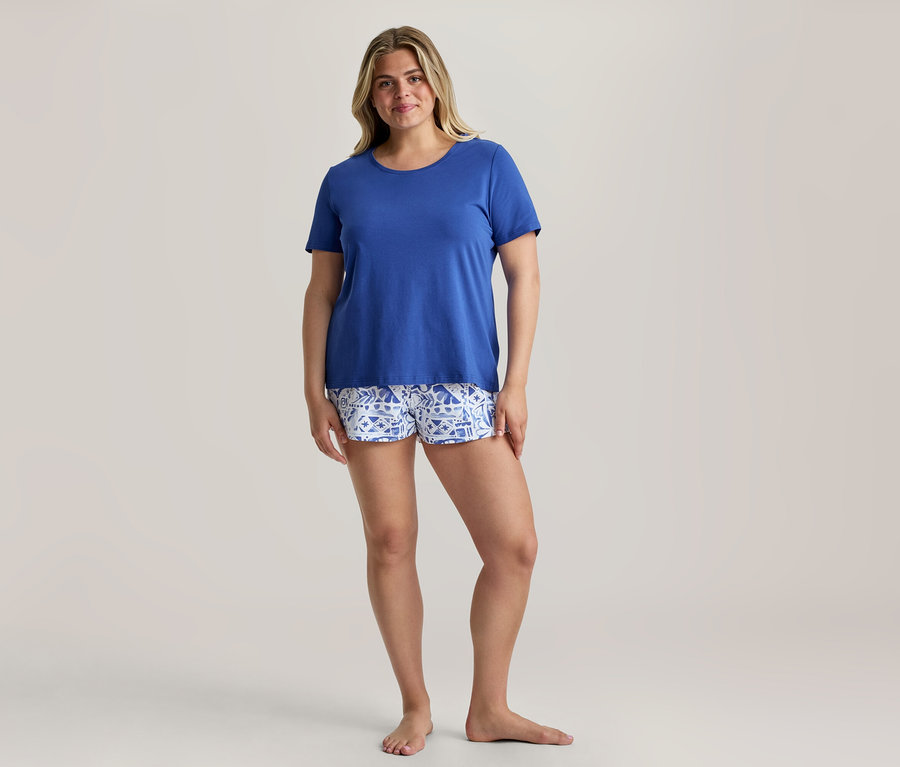 Lächelnde Frau trägt ein königsblaues T-Shirt und gemusterte Shorts von einem Shorty-Pyjama-Set.