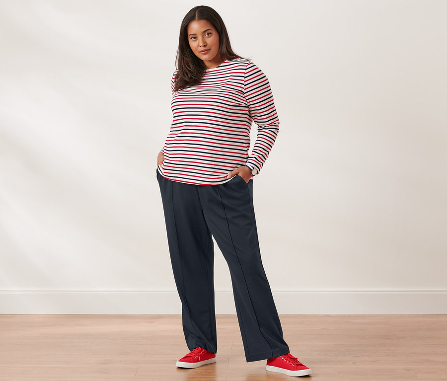 Eine Frau posiert in einem gestreiften Langarmshirt, einer Sweathose, Canvas-Sneakers und einer Quarz-Armbanduhr aus Edelstahl.