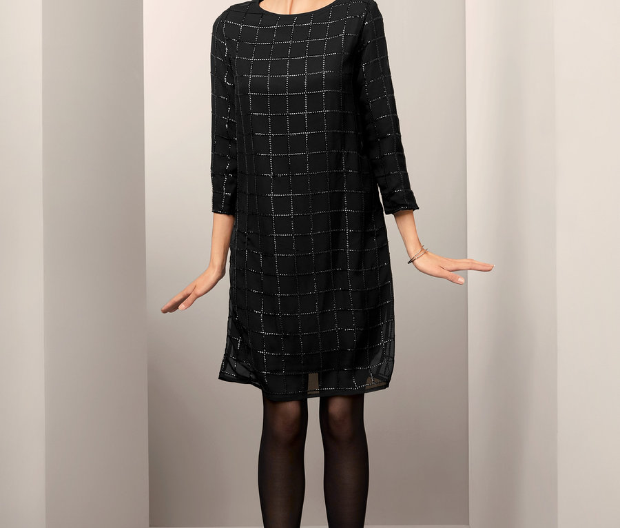 Frau steht und trägt ein festliches Kleid mit Paillettenbesatz.