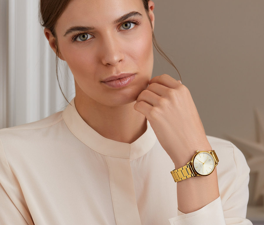 Porträt einer Frau, die eine goldfarbene Damenuhr, Edelstahl PVD-beschichtet, trägt.