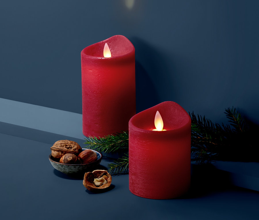 Zwei dunkelrote LED-Echtwachskerzen stehen neben Nüssen in einer Schale und Tannenzweigen.