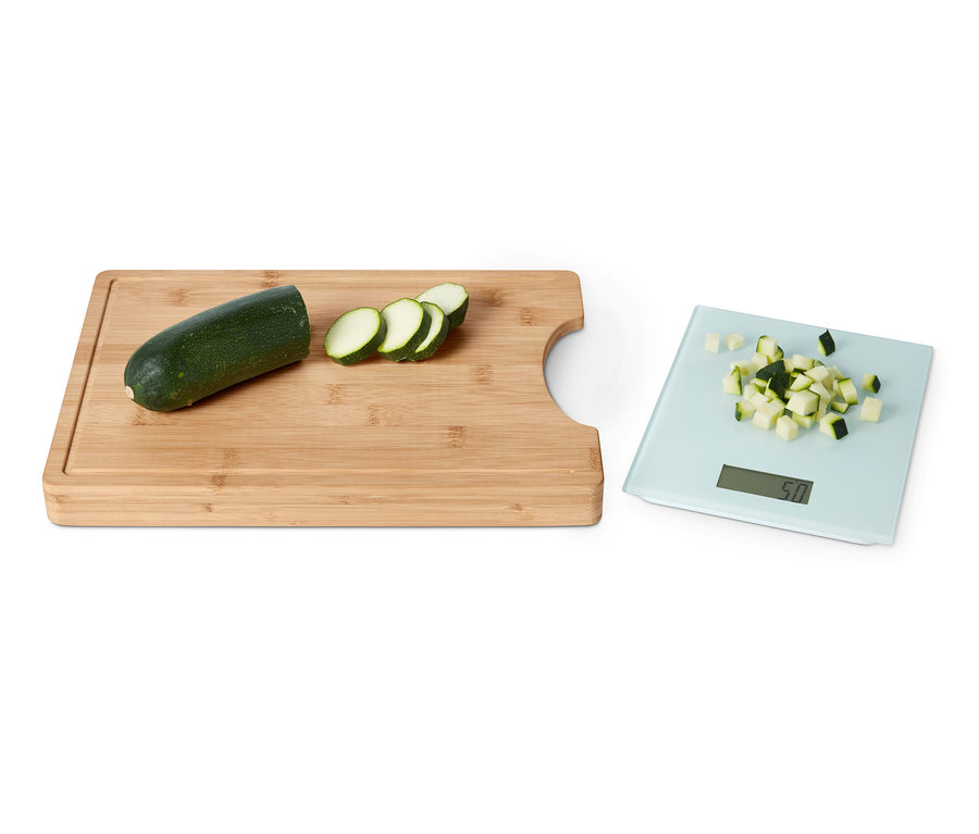 Eine grüne Zucchini, in Scheiben geschnitten, liegt auf einem Schneidebrett mit herausnehmbarer Küchenwaage. Auf der Waage befindet sich ebenfalls geschnittene Zucchini.