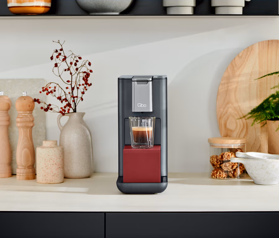 Eine Qbo ESSENTIAL Dark Berry Kaffeemaschine mit einer Tasse Kaffee auf einer Küchentheke.