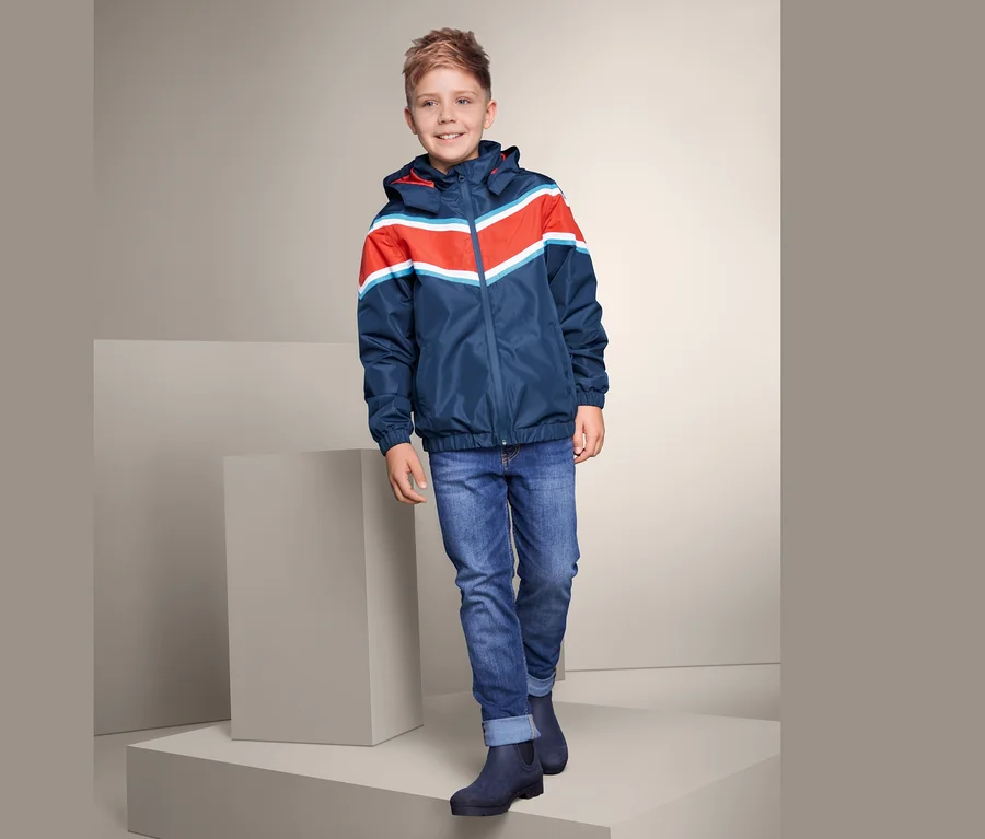 Ein Junge in Regenjacke, Jeans und Gummistiefeln steht auf einem Podest.