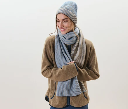 Frau lächelt und trägt einen Strickschal und eine Mütze.