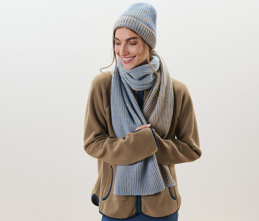 Frau lächelt und trägt einen Strickschal und eine Mütze.