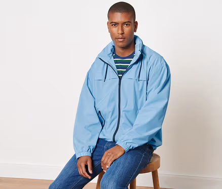 Mann sitzt auf einem Hocker und trägt eine hellblaue Windbreaker-Jacke.