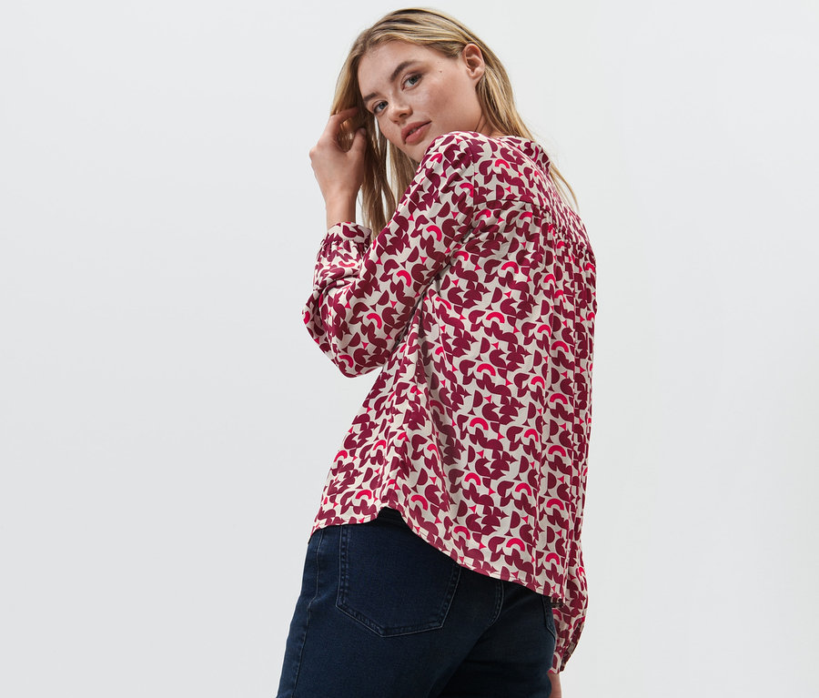 Frau blickt über die Schulter und posiert in bedruckter Bluse.