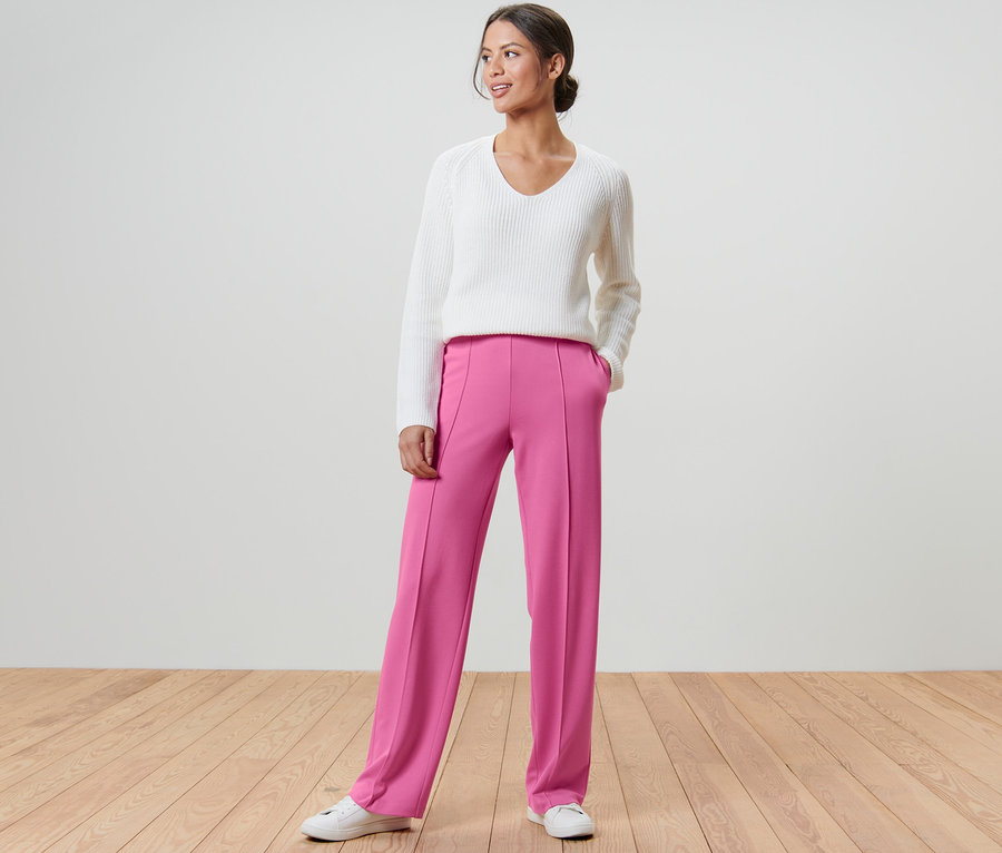 Frau posiert in pinkfarbener Jerseyhose mit Biese und weißem Pullover.