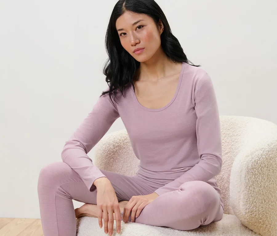 Frau sitzt auf einem Stuhl und trägt ein langes Shirt mit RWS-zertifizierter Wolle und lila Leggings.
