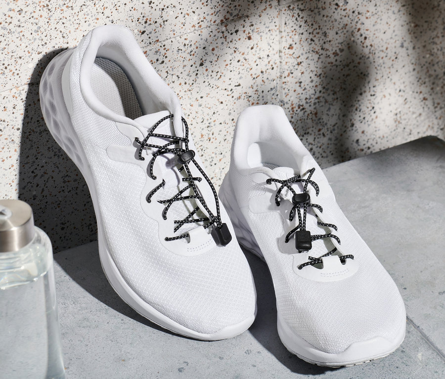 Zwei weiße Turnschuhe mit elastischen Schnürsenkeln und eine Wasserflasche.
