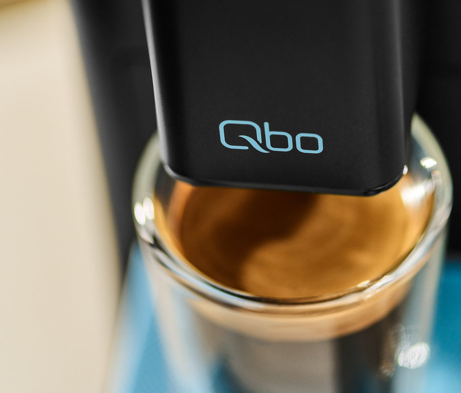 Detail einer Qbo ICONIC x Pantone Special Edition Sky Blue Kaffeemaschine, die ein Glas mit Kaffee füllt.